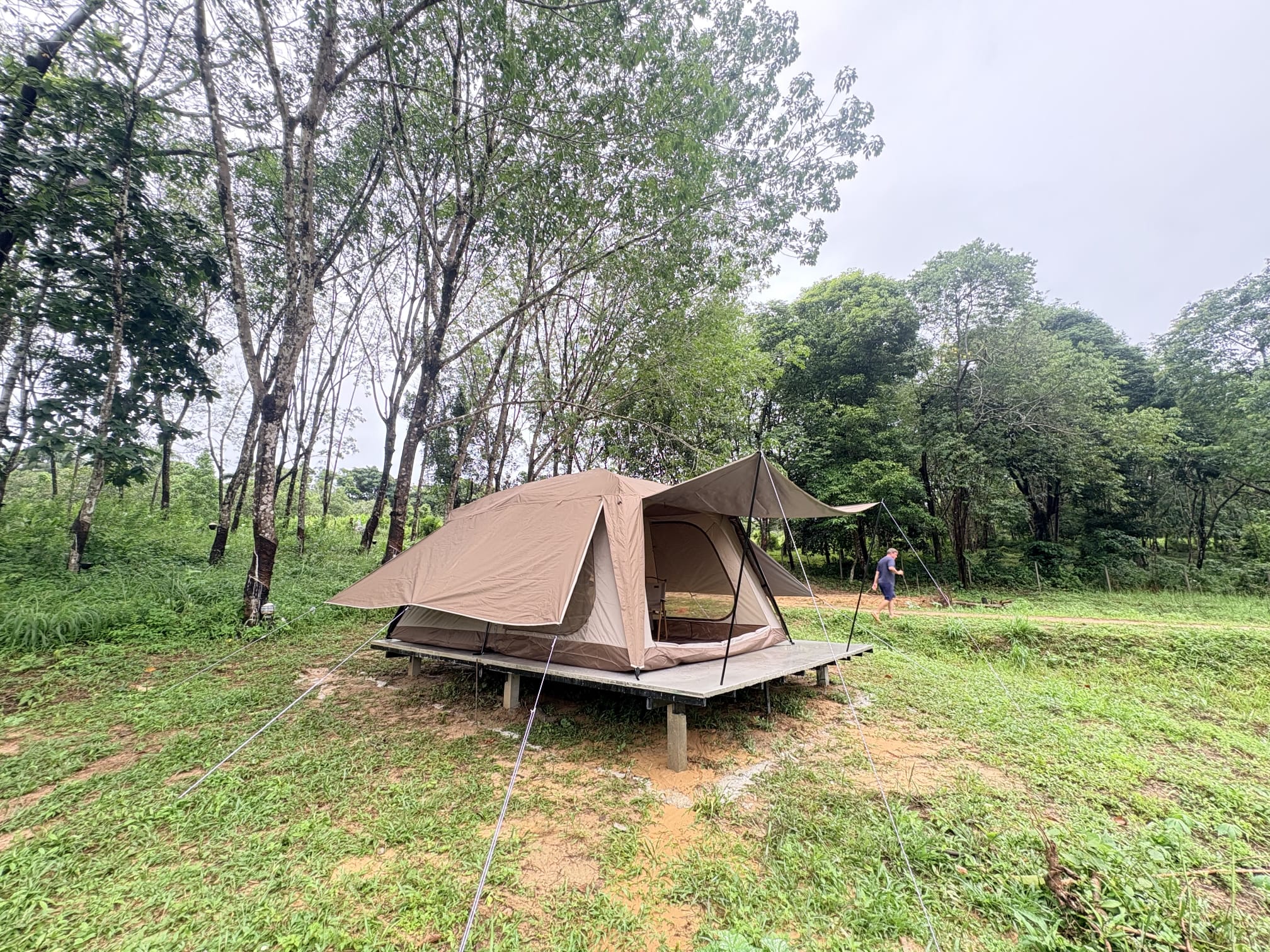 The first canvas tent on its raised concrete platform seen from the side, porch awning out, with a man walking along the track behind it