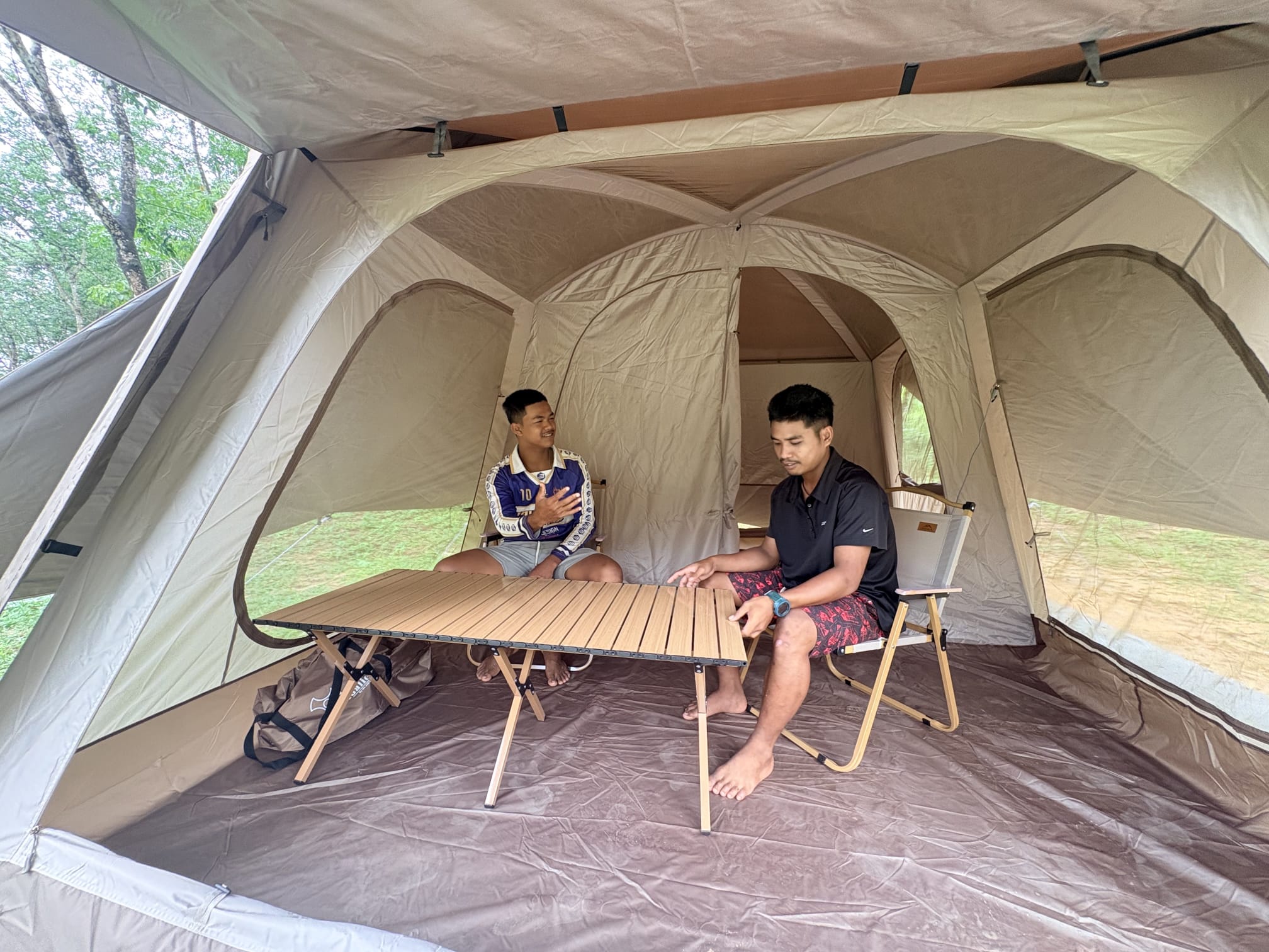 Two young men sitting at a folding wooden table on camp chairs inside the newly furnished tent
