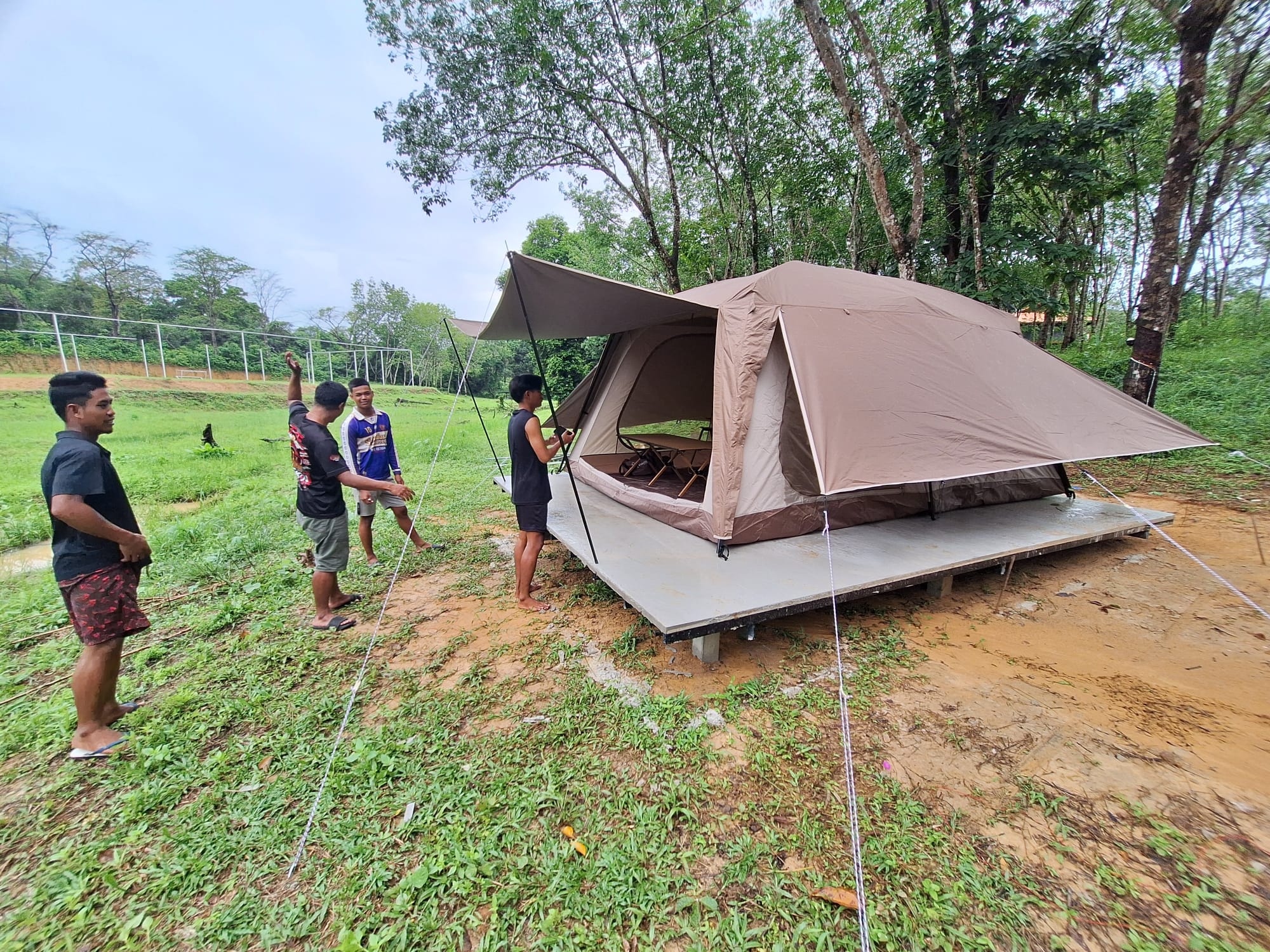 The example tent for the new tourist tent camp on its raised deck, with four young men on the grass beside it and the netted fence of the soccer field behind
