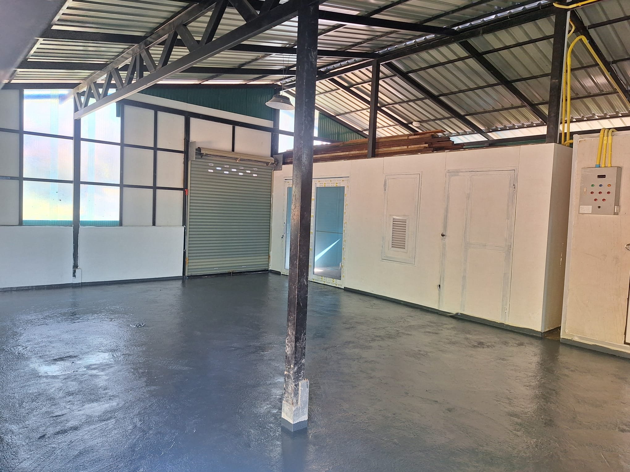 Inside the steel-roofed factory shed: a freshly coated grey floor, white partitioned rooms with doors and windows, a roller shutter and an electrical control box