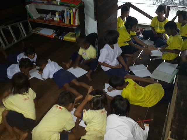 Moken children doing schoolwork together inside the enlarged wooden house