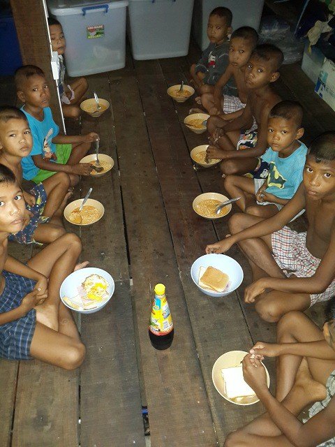 Moken children sharing a meal down a long wooden table in the house