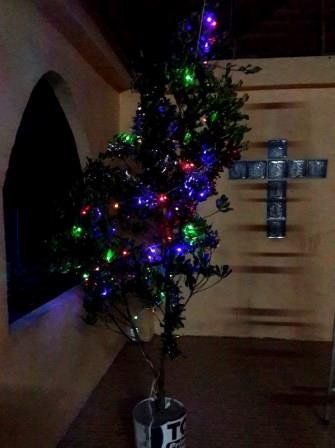 A small Christmas tree with coloured lights beside a handmade cross in the island church