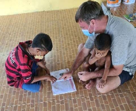 Philip helping two Moken boys follow the text during a reading lesson