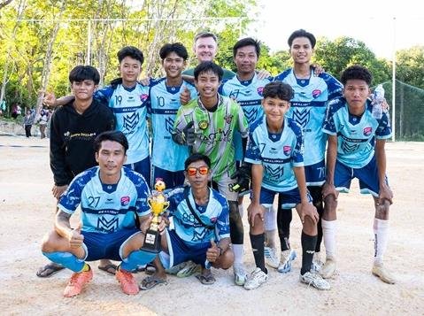 The island soccer team in their blue kit posing with a trophy, Philip at the back