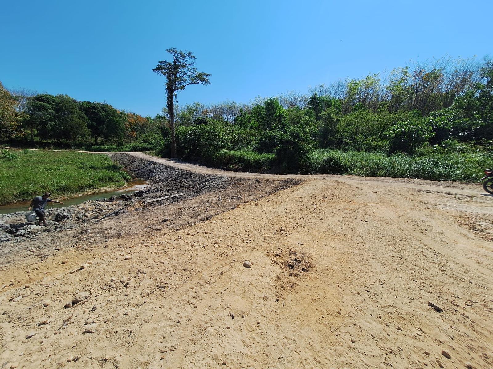 The newly built dirt road to the soccer field, running beside a stream through the bush under a clear blue sky