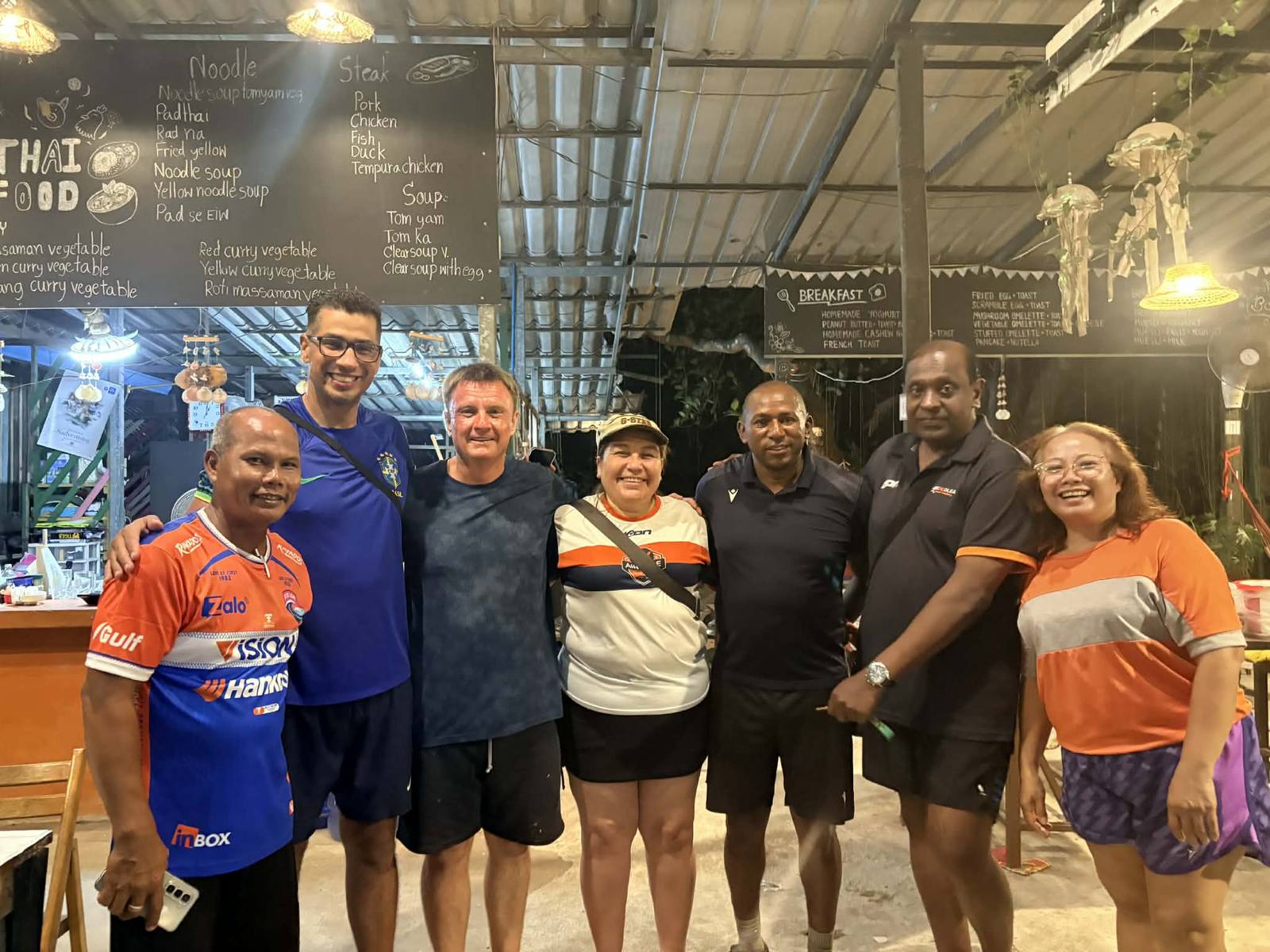 Visitors from Beram's football team with local hosts, together at night in an open-air Thai restaurant
