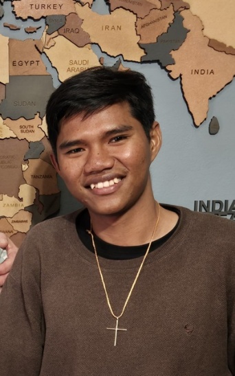 Wud smiling in front of a wooden world map before writing the water-operator test in Suratthani